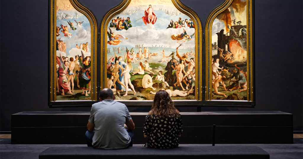 two people sitting on bench looking at painting of angels and demons