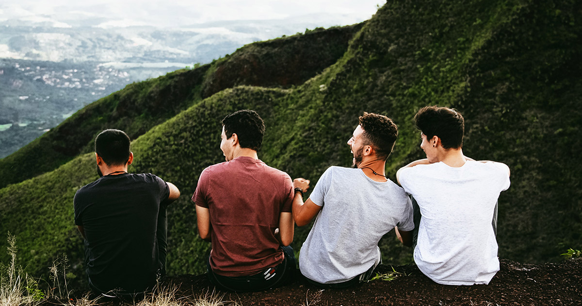 four friends sit in front of view of the mountains